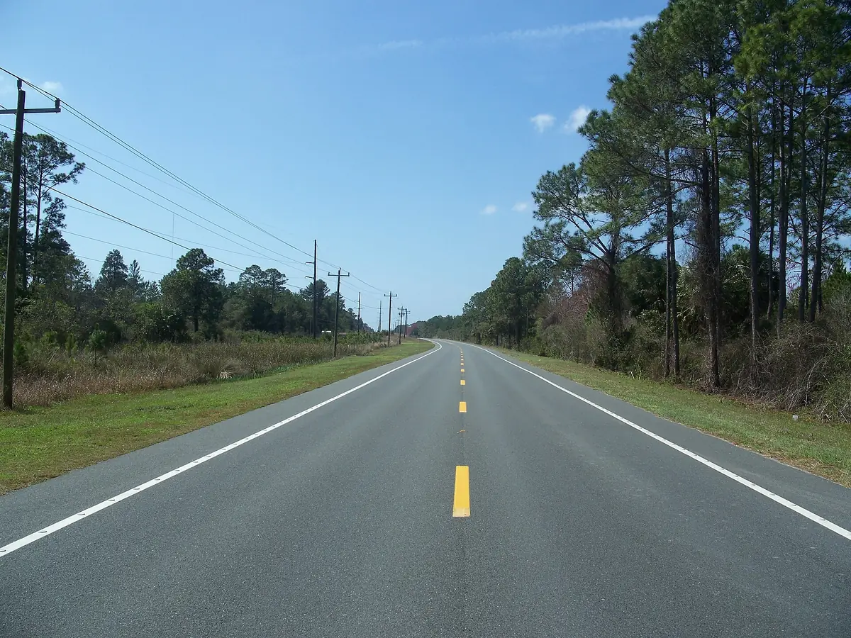 Two-lane SR 24 running straight through tall pines toward Cedar Key under a clear blue sky