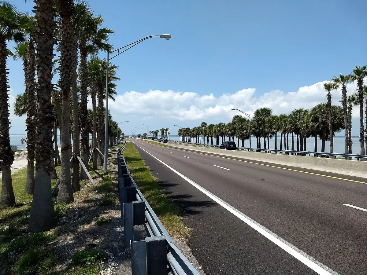 Palm-lined Courtney Campbell Causeway running beside Old Tampa Bay on a bright day