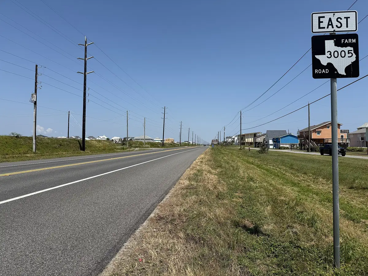 Two-lane FM 3005 running straight along the west end of Galveston Island under a clear sky