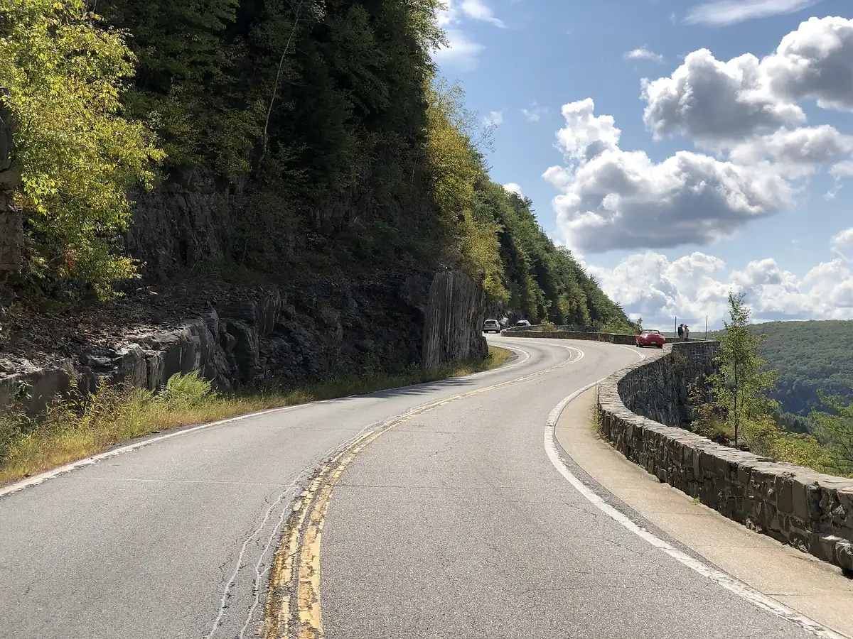 NY 97 curving past a rock cut and stone wall high above the Delaware River at Hawk's Nest
