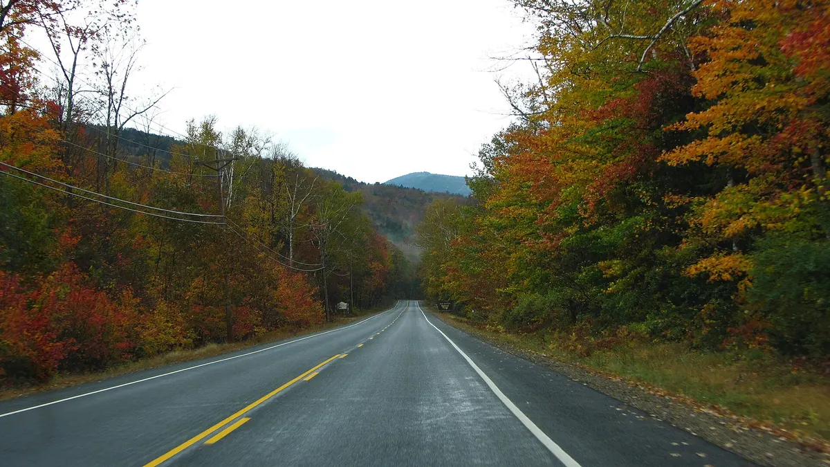 Kancamagus Highway running between red and orange fall trees toward a mountain near Lincoln, New Hampshire