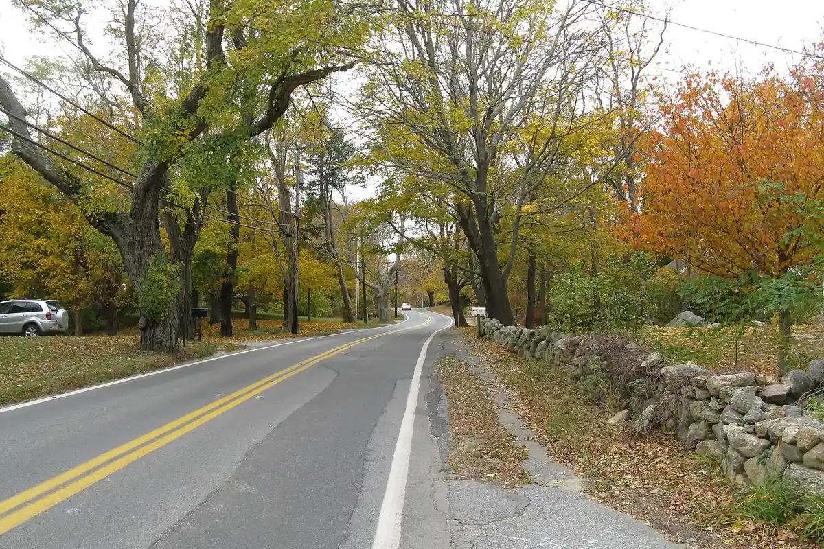 Route 6A, the Old King's Highway, curving past a stone wall under autumn trees in West Barnstable